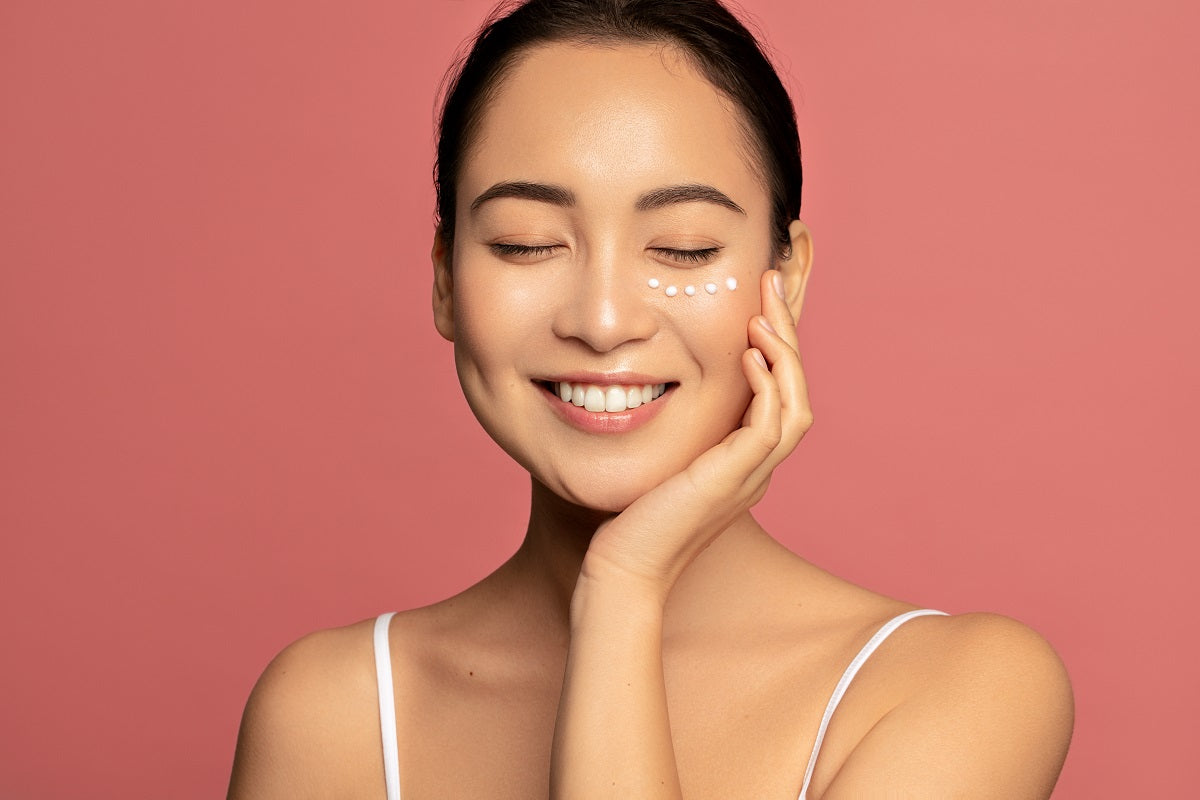 Young Beautiful model posing against pink background with applied cream under her eyes.