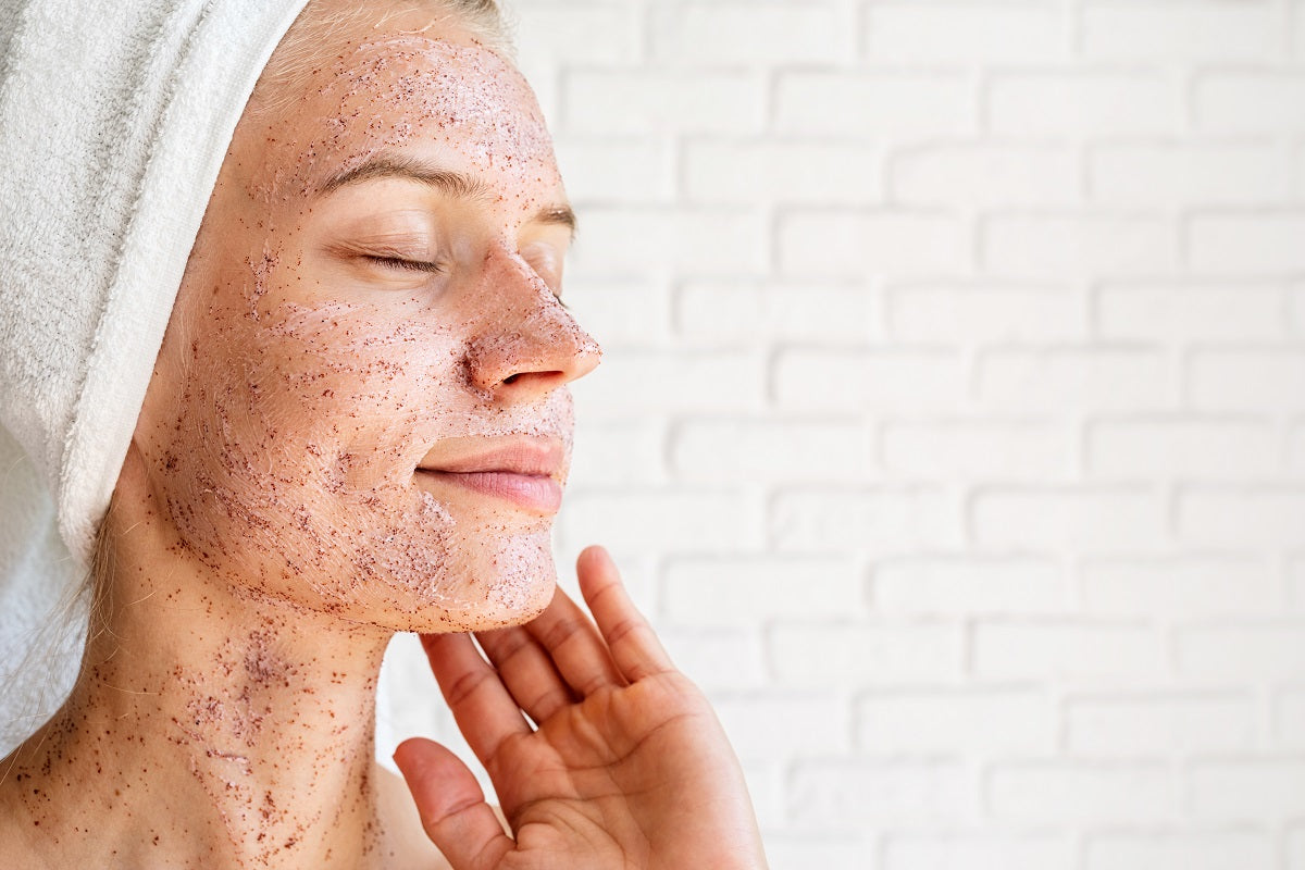Close up shot of attractive smiling woman applying scrub on her face skin