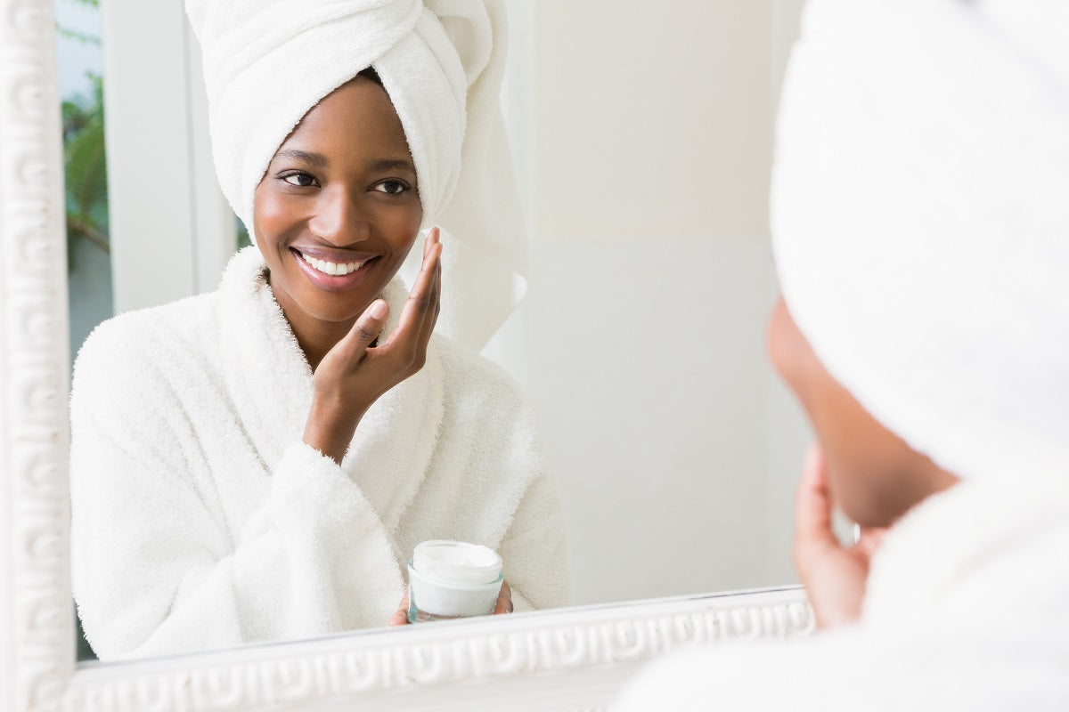 Young woman applying moisturizer to her skin in the bathroom